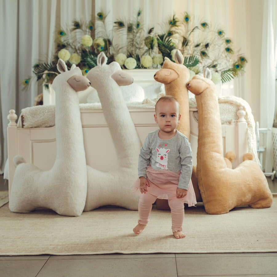 Child standing between giant beige and rust plush alpacas – full size comparison in children's room