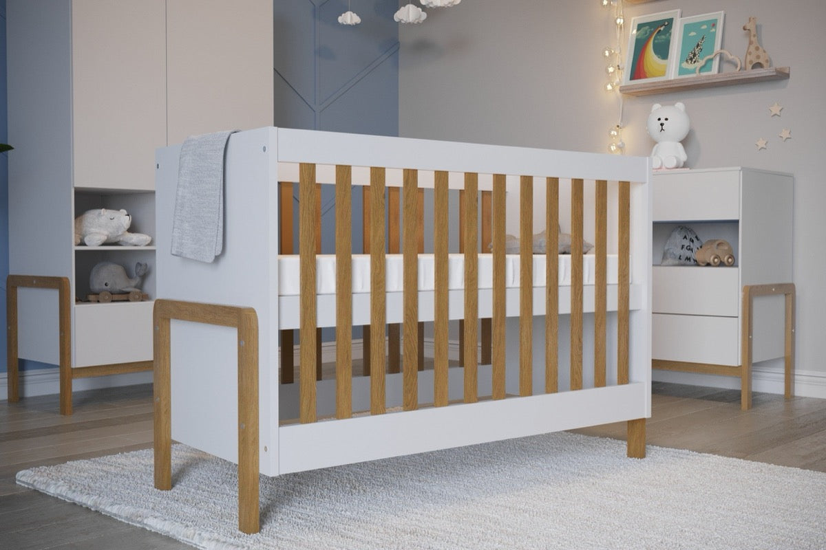 Victor crib positioned in nursery with matching white storage unit and oak accents