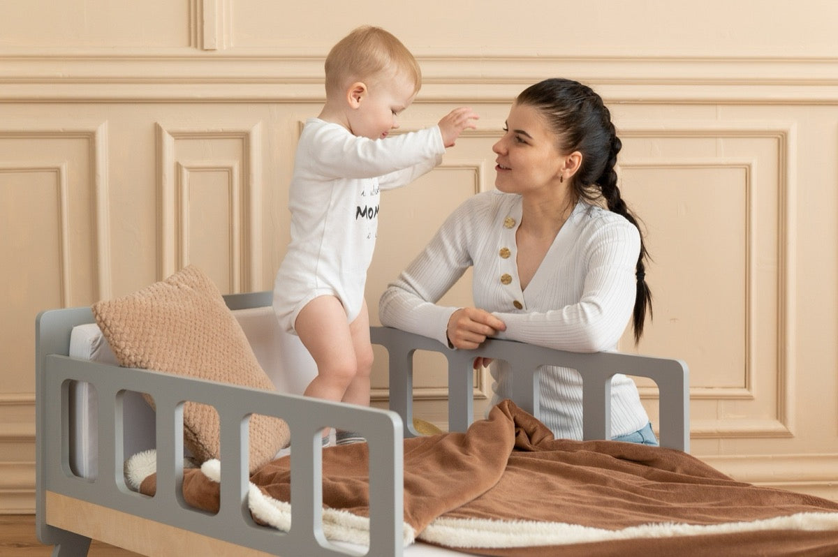 Baby standing on gray Family-scl growing bed with mother – safe toddler bed with sturdy safety rails for babies
