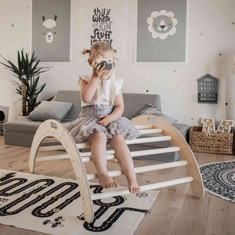 Girl sitting on wooden climbing arch used as rocker in playroom setting