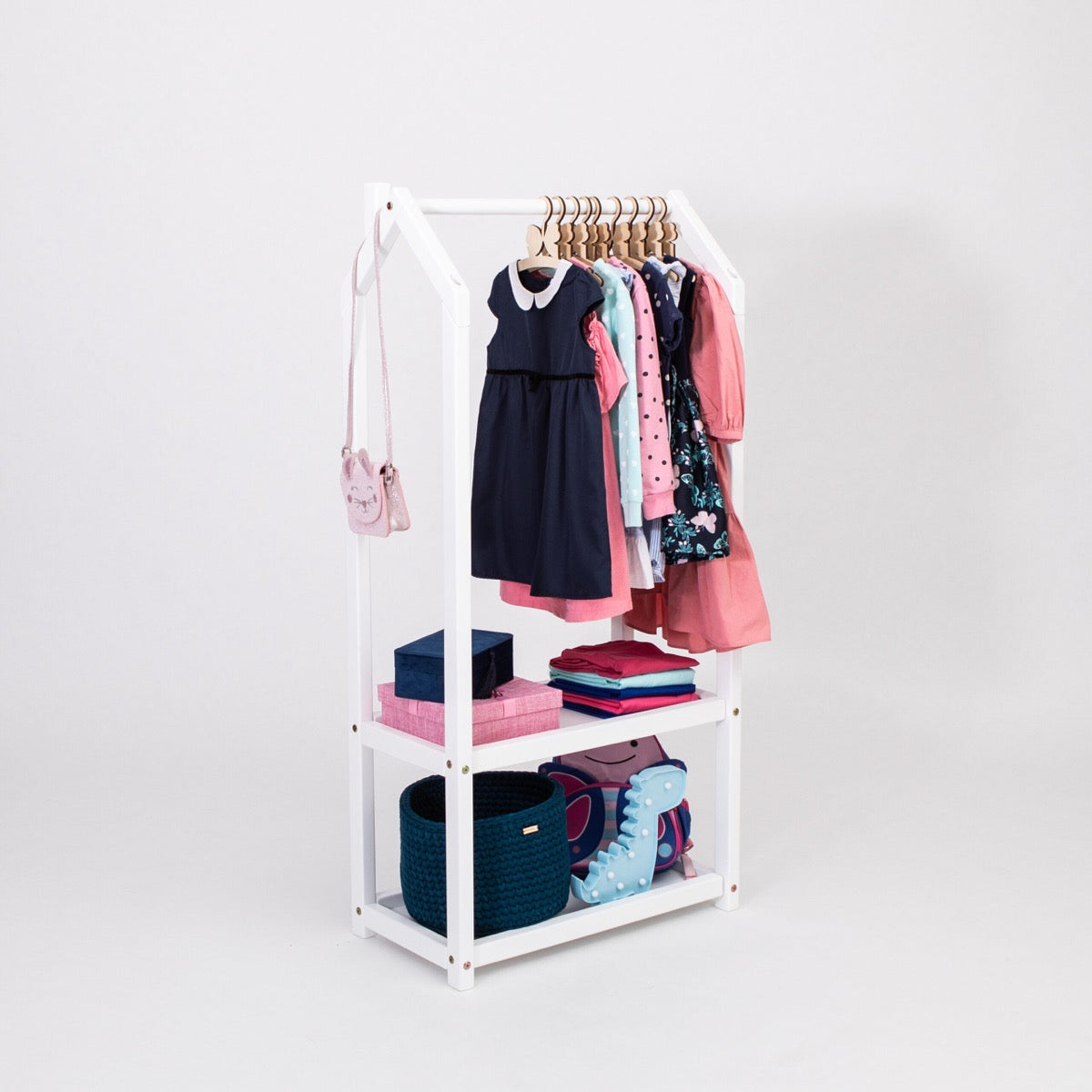 White house-shaped clothing rack with hanging children's dresses and folded items on shelves