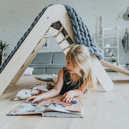 Girl reading under draped climbing triangle creating cozy play tent space
