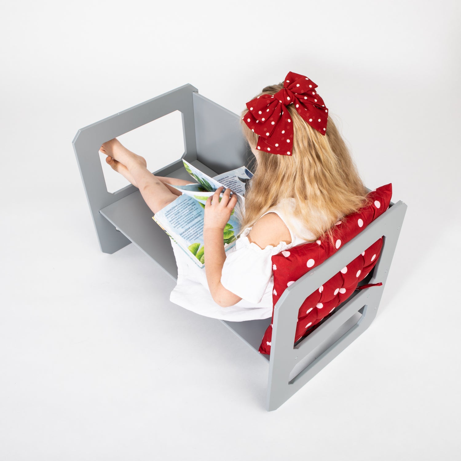Young girl in white shirt reading at gray Montessori weaning table with red polka dot chair cushion