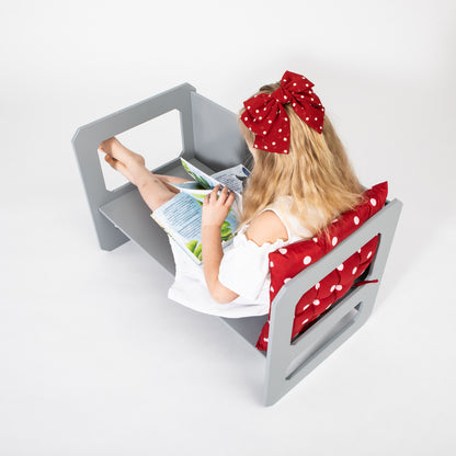Young girl in white shirt reading at gray Montessori weaning table with red polka dot chair cushion