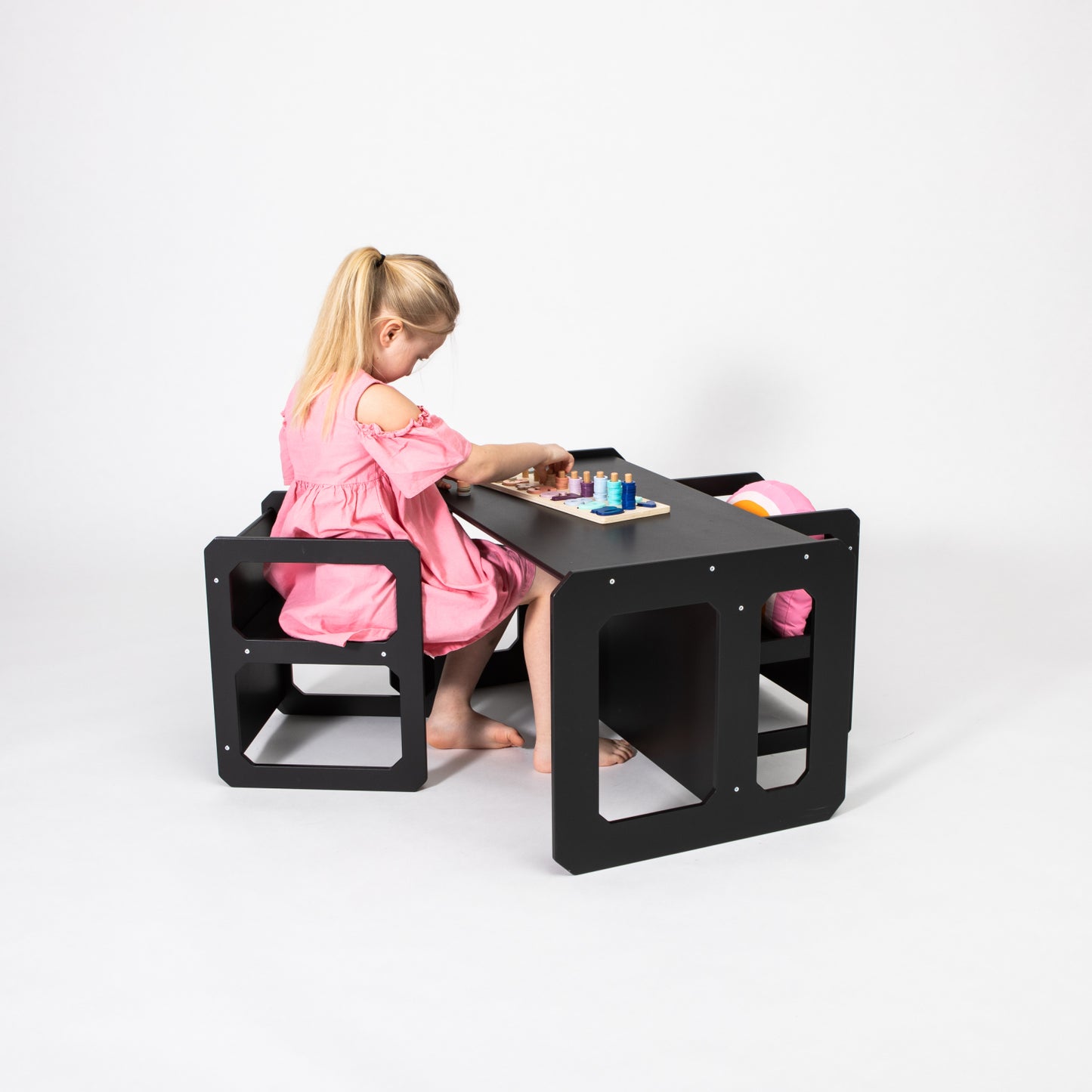 Child in pink dress seated at black Montessori table and chair set playing with toys