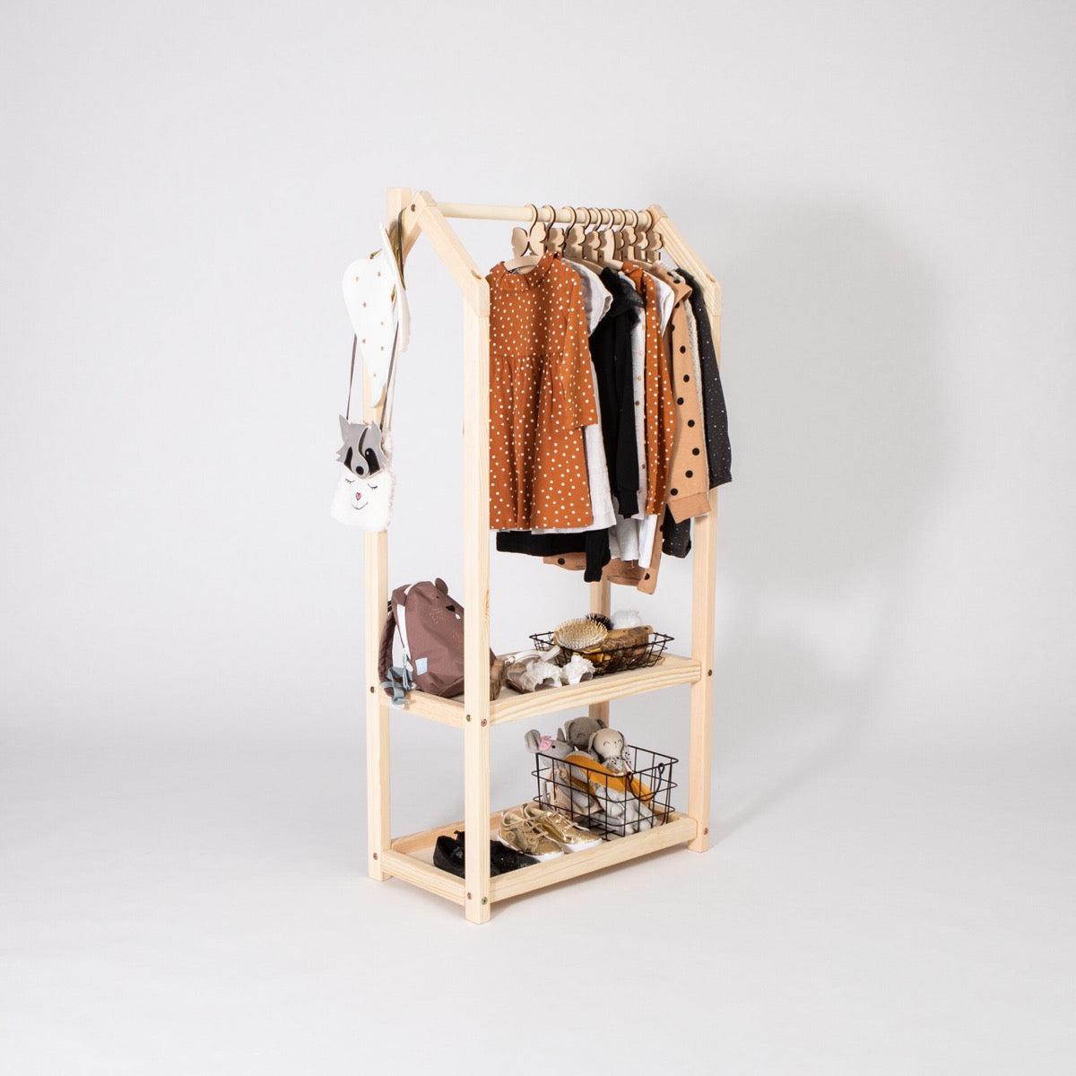 Natural wood house-shaped clothing rack with brown children's clothing hung on rod and baskets on shelves