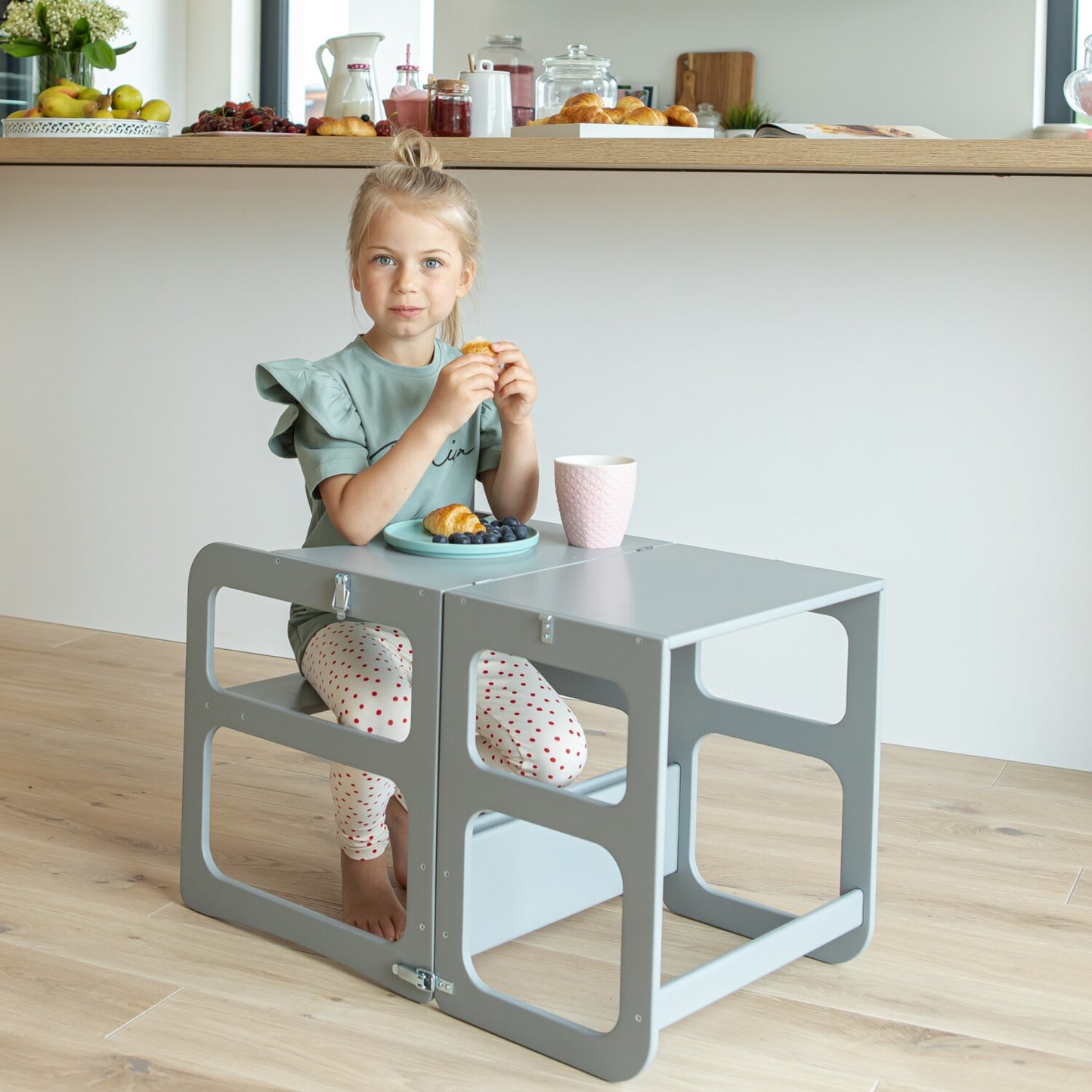 Child sitting at gray Montessori kitchen tower table with storage compartments