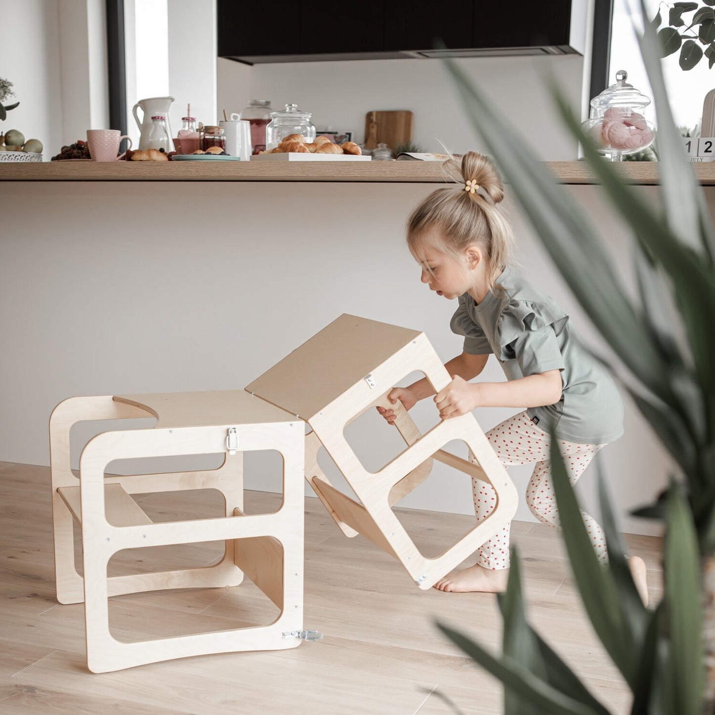 Child opening fold-down desk top on white convertible kitchen tower furniture