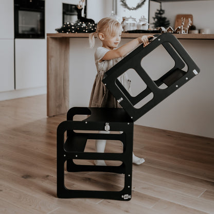 Child stacking black kitchen tower step stool sections to demonstrate transformation