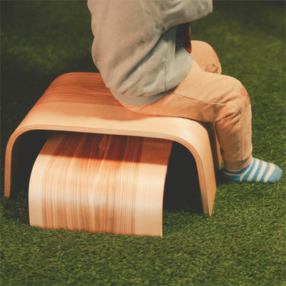 Child stepping on single wooden step stool on grass outdoors
