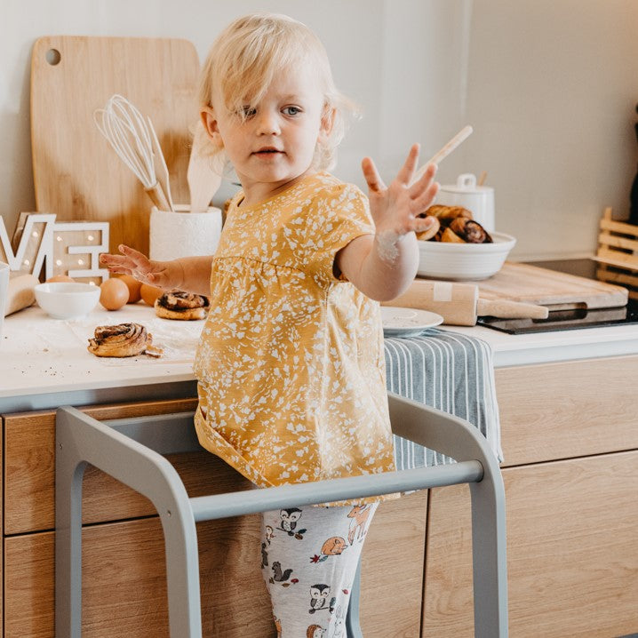 Child on white step stool reaching counter independently with toys and cooking utensils
