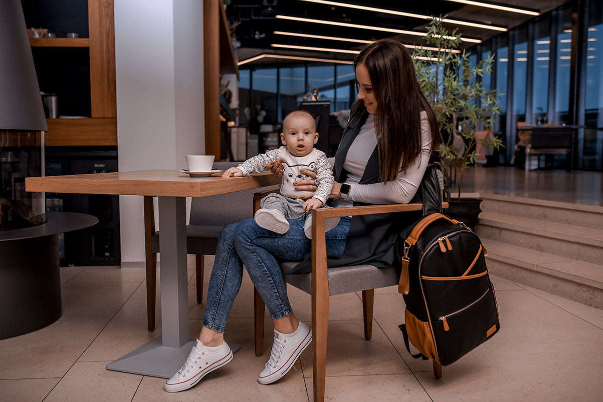 Mother with toddler at table with black coffee diaper backpack on chair beside them