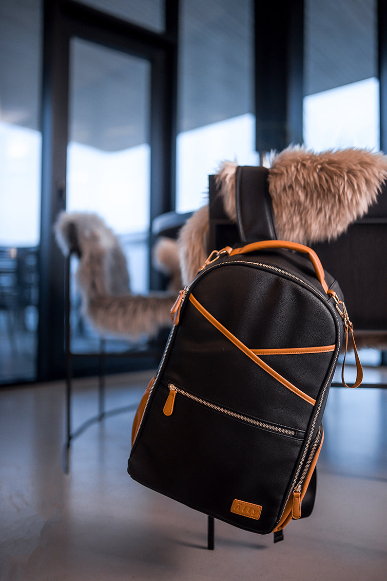 Black coffee diaper backpack displayed on chair in modern minimalist interior setting