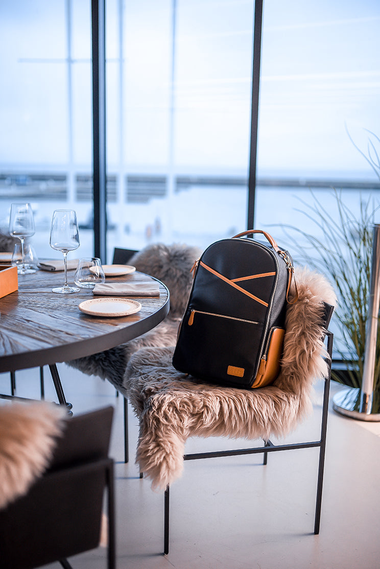 Outdoor dining scene with large vegan leather diaper backpack on white fur throw chair