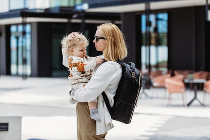 Mother holding toddler while wearing espresso Scandic diaper backpack outdoors