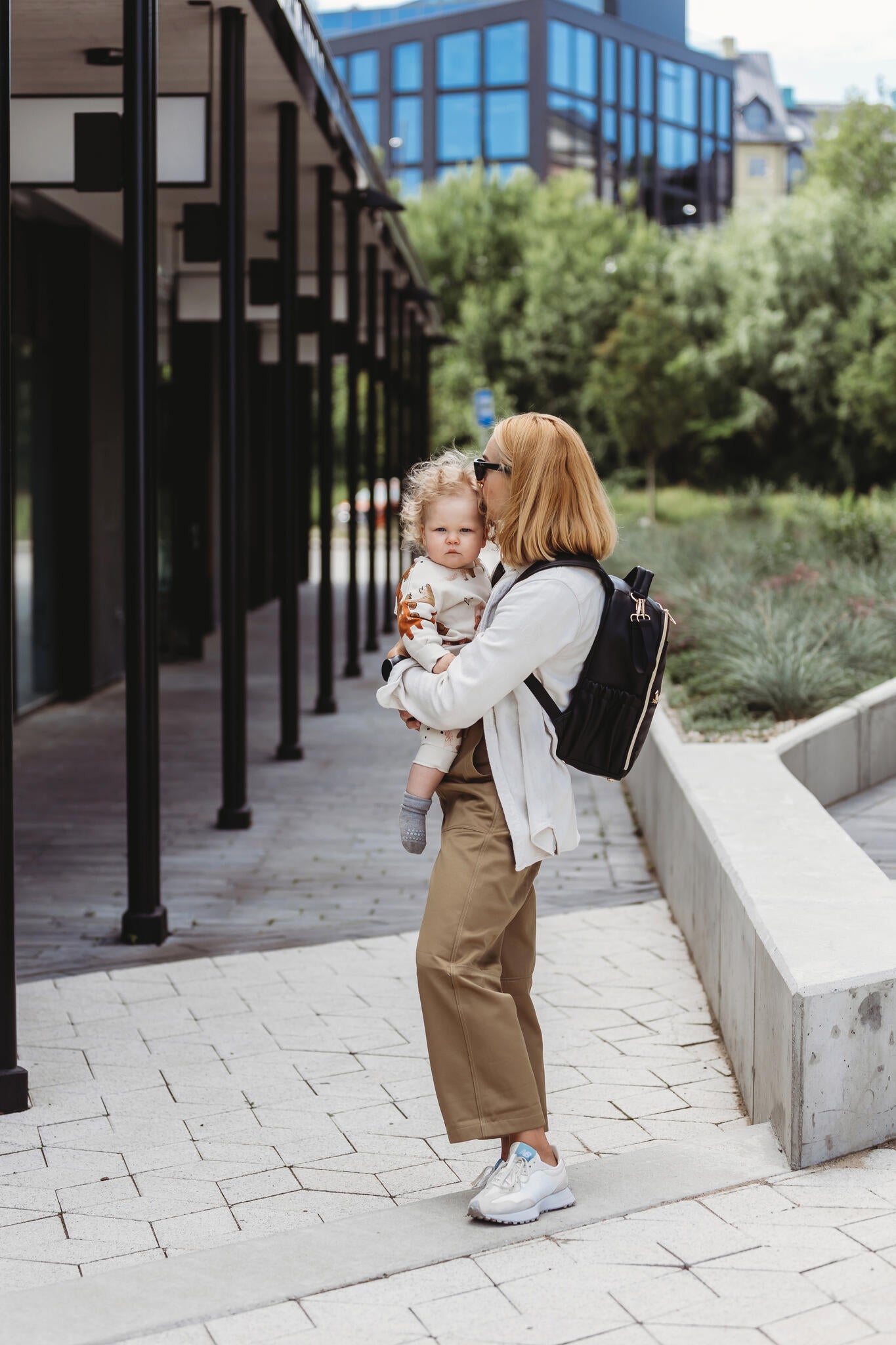 Mother wearing black Ally Scandic diaper backpack holding toddler