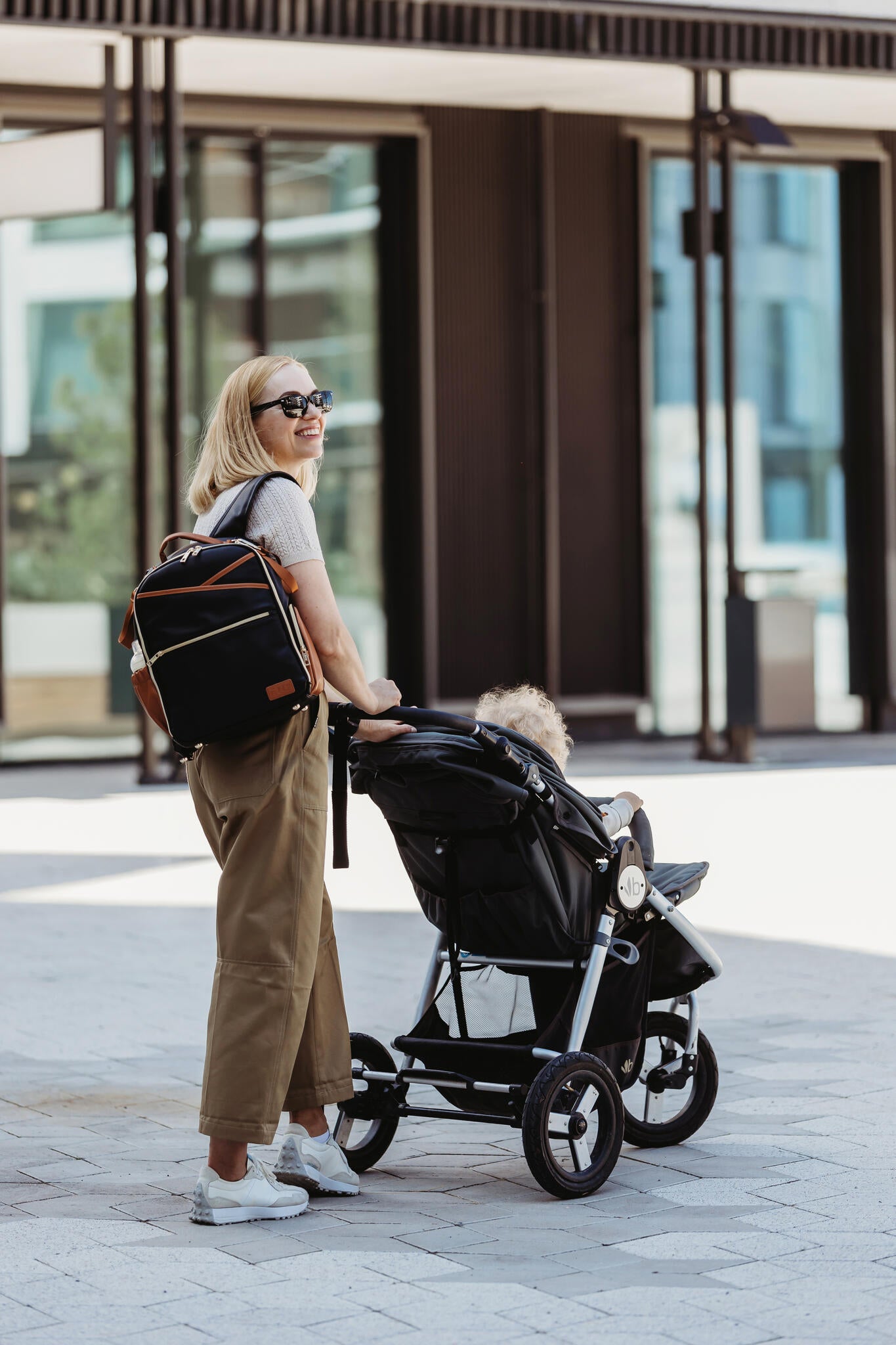 Parent carrying child while holding small diaper backpack near stroller