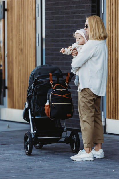 Diaper backpack hanging from stroller bar near water