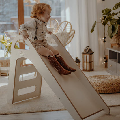 Child sliding down white wooden slide with rope handholds in Scandinavian nursery