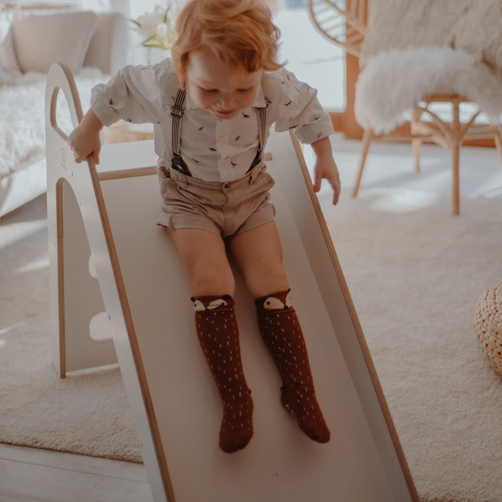 Young child mid-slide on white wooden play slide viewed from side angle