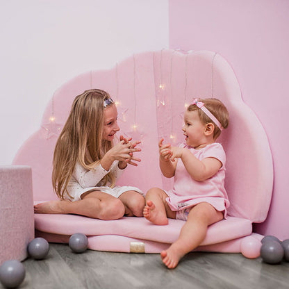 Two children sitting inside pink cloud shaped play mat with warm lighting