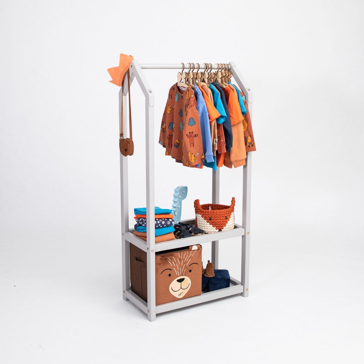 Gray house-shaped clothing rack displaying hanging children's clothing and storage baskets on shelves