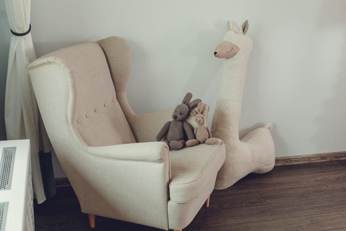 Beige oversized stuffed alpaca plush toy – nursery corner with armchair and soft toys
