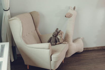 Beige oversized stuffed alpaca plush toy – nursery corner with armchair and soft toys
