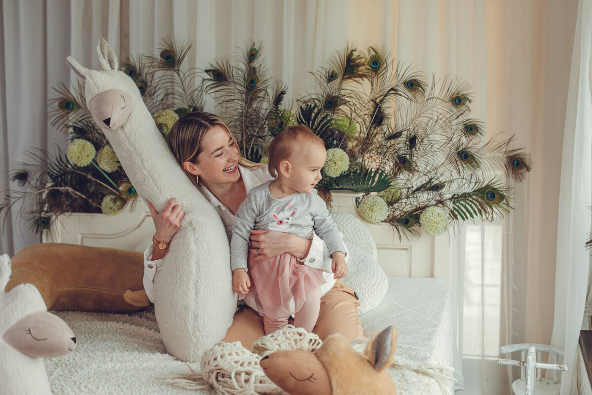 Mother and baby enjoying giant plush alpaca toy Kai aš mažas buvau – lifestyle play scene
