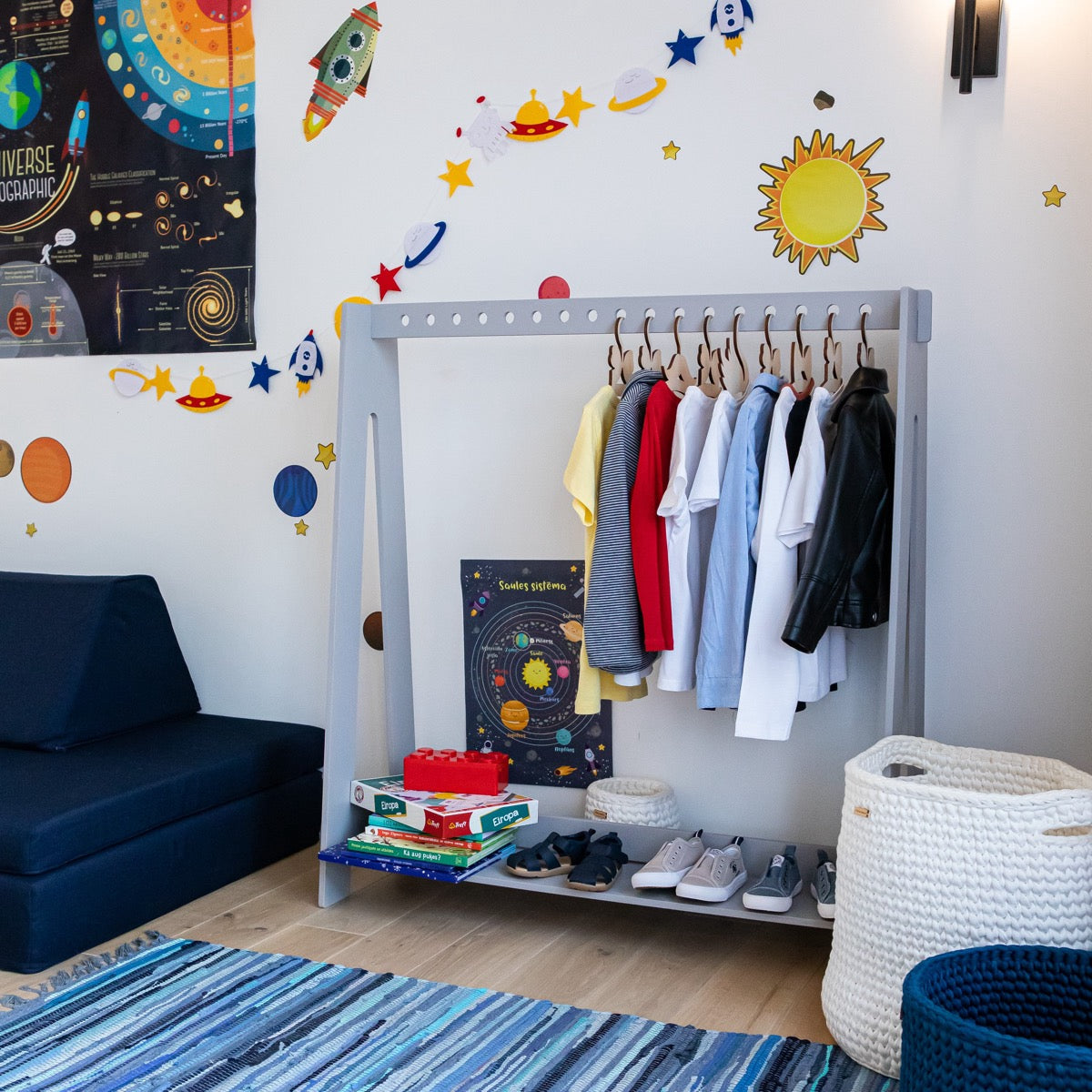 Grey Montessori clothing rack in space-themed nursery with clothes and storage baskets