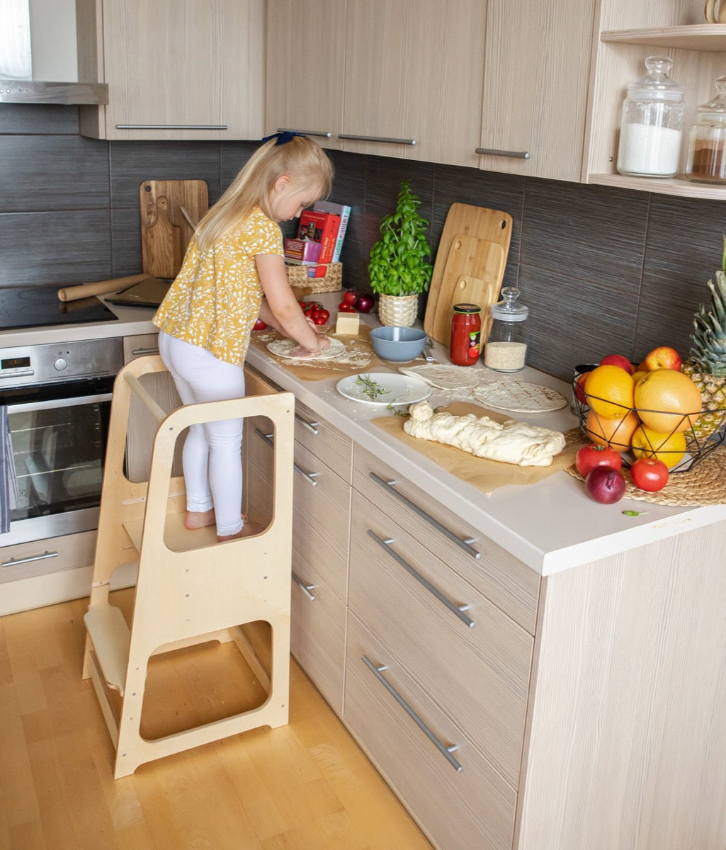 Toddler on light blue step stool preparing dough with adult guidance in kitchen