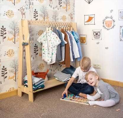 White wooden children's clothing rack with neutral outfit selection and toy storage