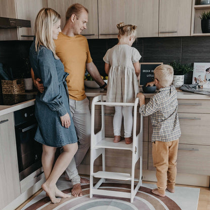 Family of four in kitchen with child using white learning tower at counter