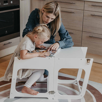 Child using white Montessori kitchen tower while adult supervises in modern kitchen