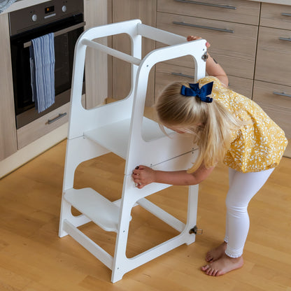 Child bending over white kitchen tower table while cooking in modern kitchen