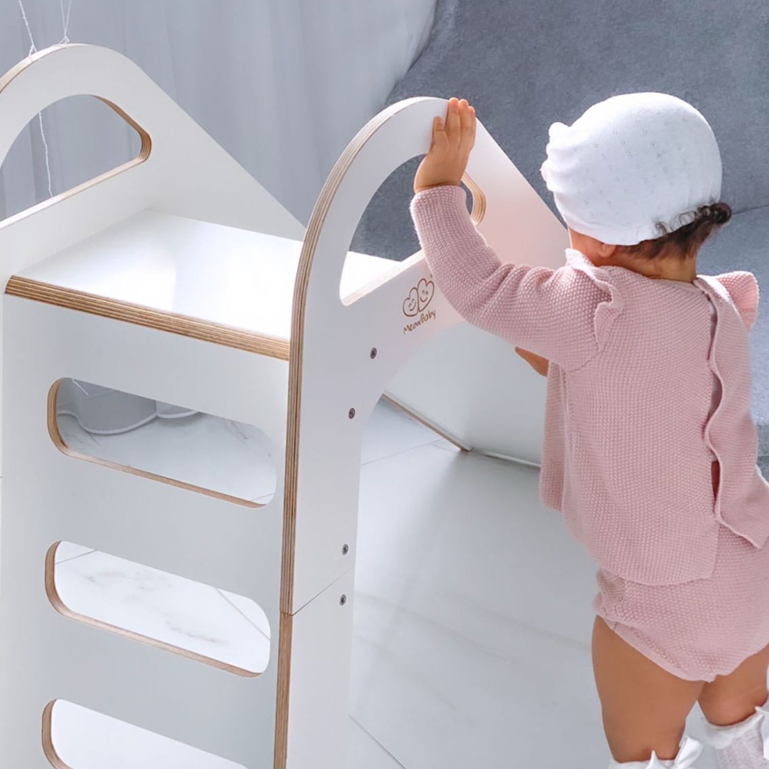 Toddler climbing white wooden slide's ladder in contemporary playroom setting