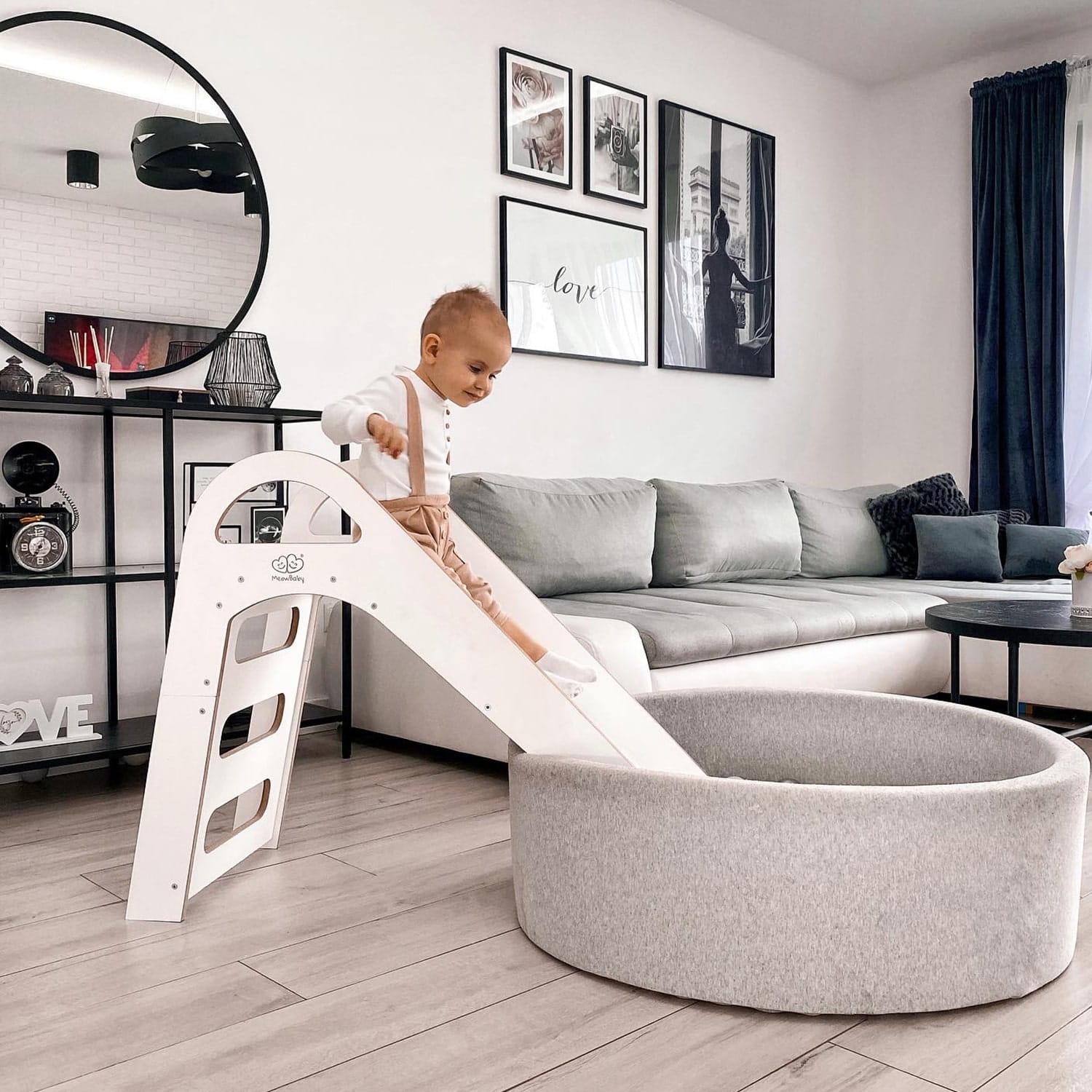 Baby navigating wooden Scandi slide in modern living room with sofa