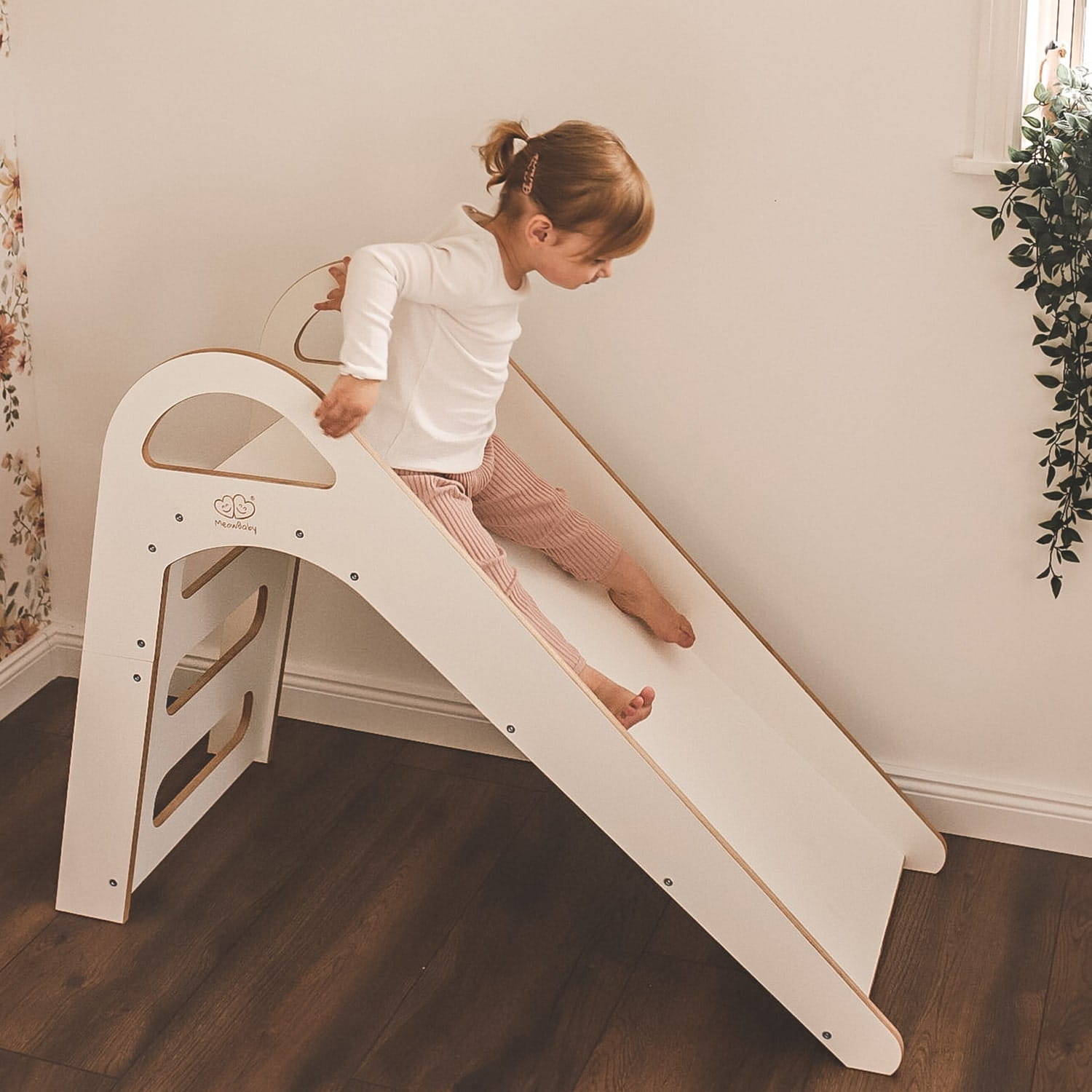 Girl sliding down white wooden Scandi slide with rope grip in modern home