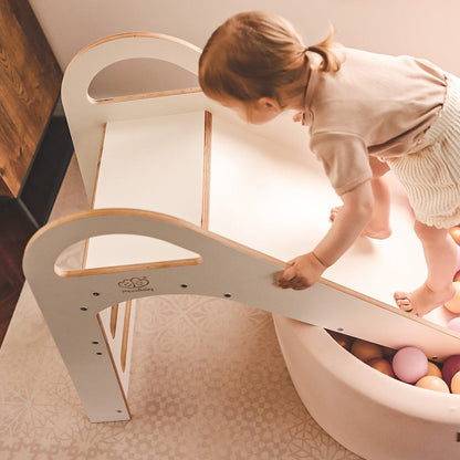 Toddler sliding into ball pit basin attached to wooden indoor slide