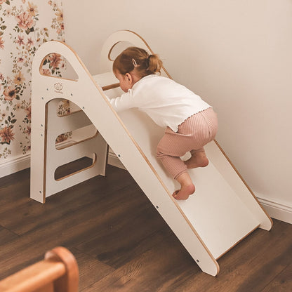Child playing in colorful ball pit below white wooden Scandi slide