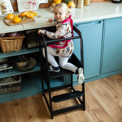 Toddler standing on gray helper tower stool preparing food at kitchen counter