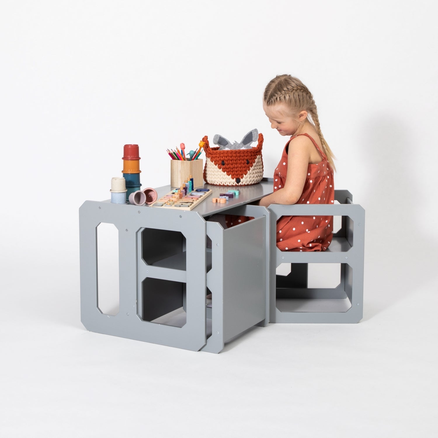 Child in coral dress using gray Montessori weaning table and chair set with art supplies and toys