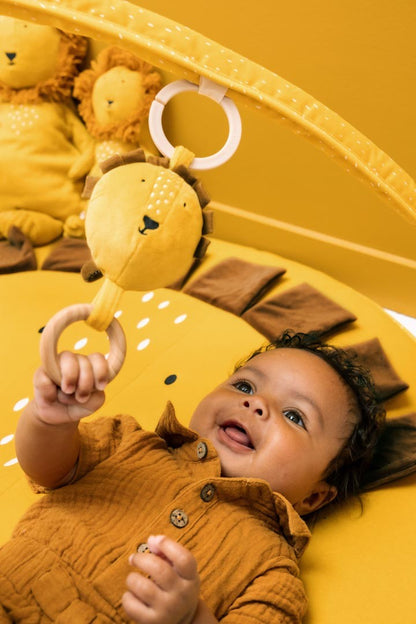 Baby playing on yellow lion mat, reaching for hanging wooden ring toy