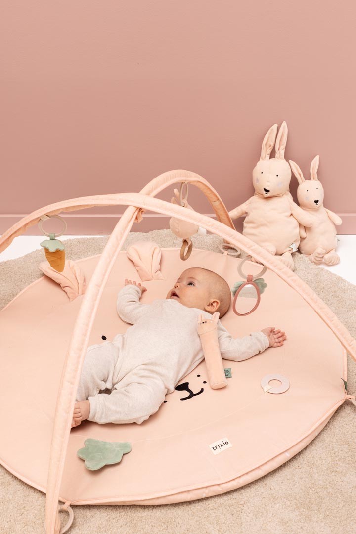 Baby playing on Mrs. Rabbit activity gym with arches, hanging toys, and stuffed rabbits nearby