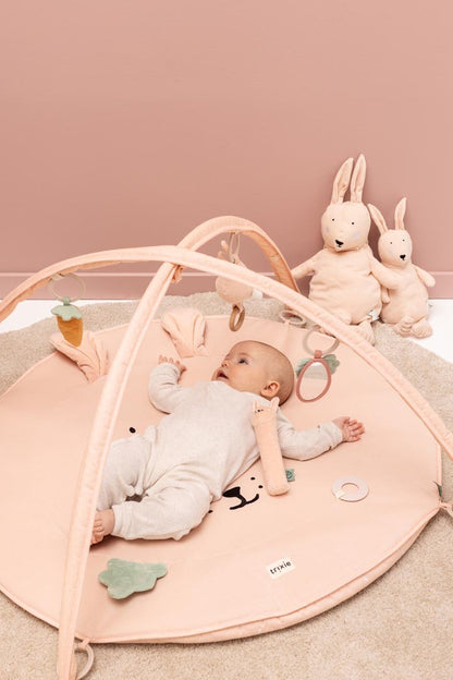 Baby playing on Mrs. Rabbit activity gym with arches, hanging toys, and stuffed rabbits nearby