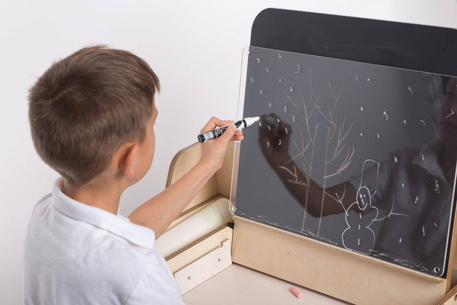 Child drawing on chalkboard panel attached to Montessori workspace table