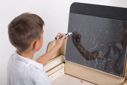 Child drawing on chalkboard panel attached to Montessori workspace table