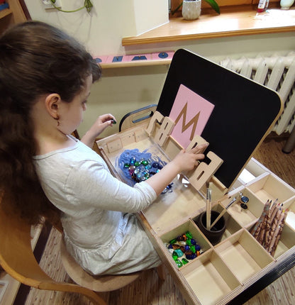 Child organizing colorful beads and materials in compartments of Montessori table