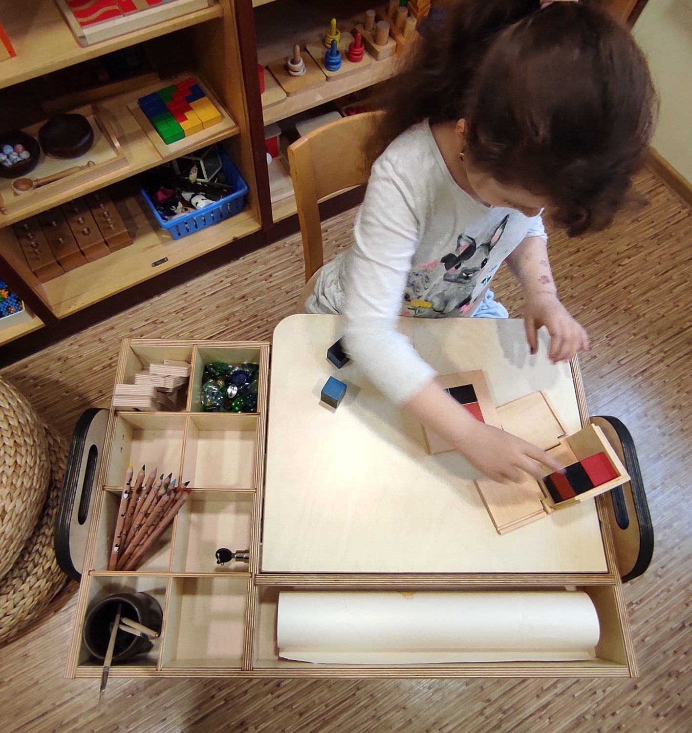 Child working at Montessori table with organized compartments for art supplies and materials