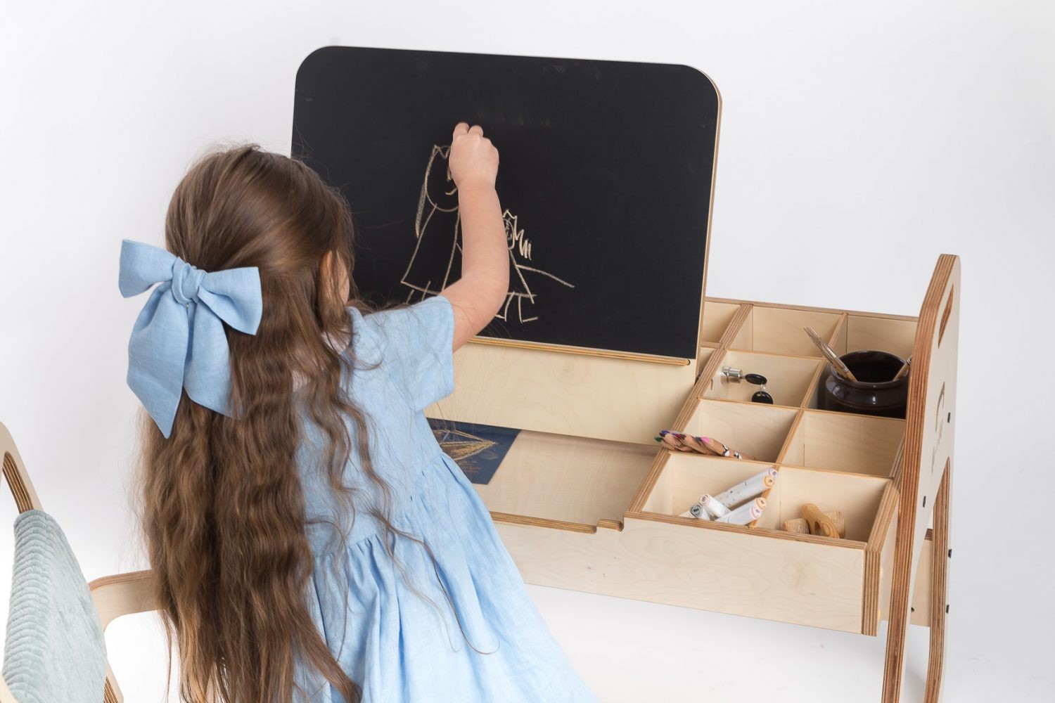 Girl writing on chalkboard panel with storage cubbies visible on Montessori table